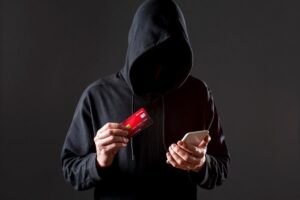 Mężczyzna-haker w kapturze trzymający smartfon i kartę kredytową