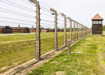 Widok obozu koncentracyjnego Auschwitz-Birkenau z charakterystycznymi barakami i ogrodzeniem z drutu kolczastego.
