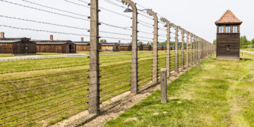 Widok obozu koncentracyjnego Auschwitz-Birkenau z charakterystycznymi barakami i ogrodzeniem z drutu kolczastego.