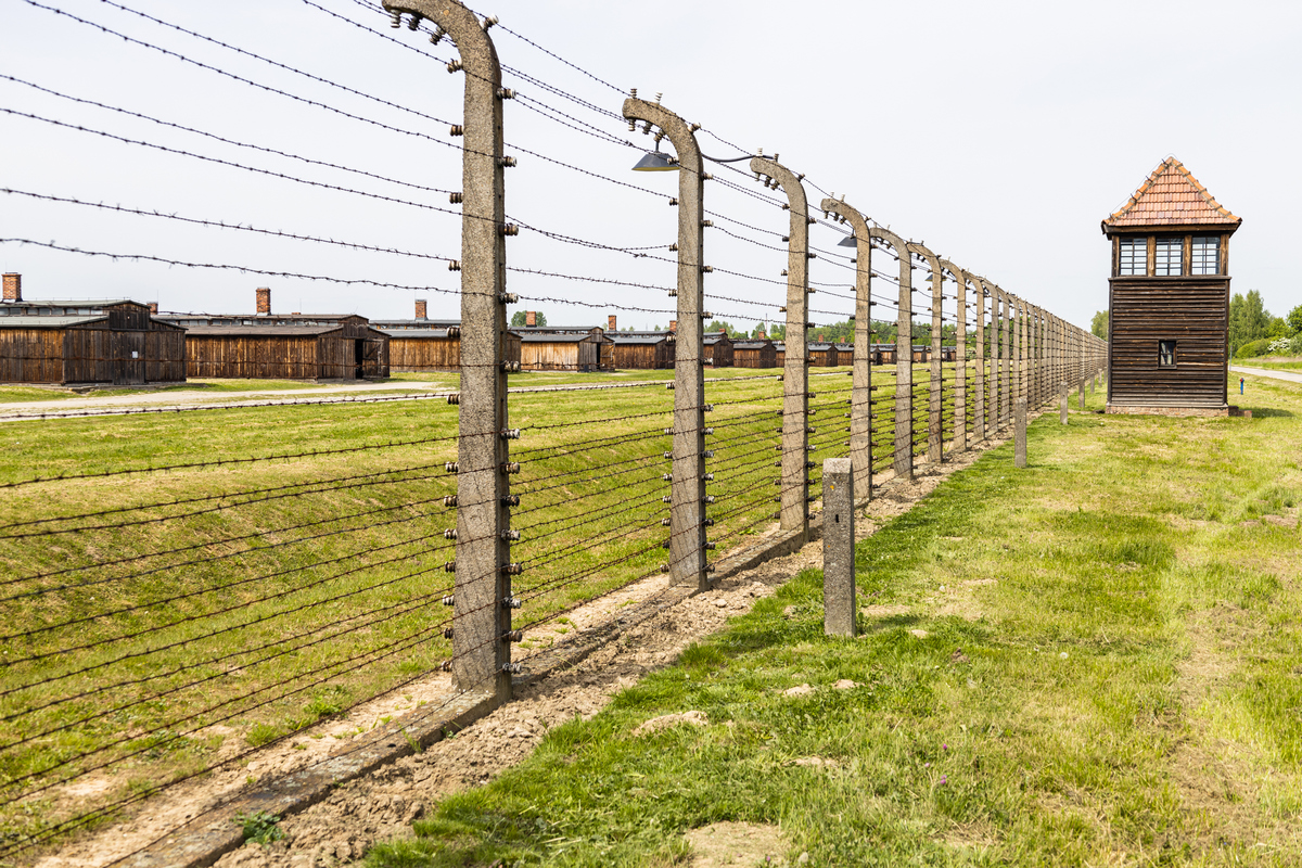 Widok obozu koncentracyjnego Auschwitz-Birkenau z charakterystycznymi barakami i ogrodzeniem z drutu kolczastego.