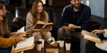 Grupa młodych ludzi z książkami siedzących przy stole z kawą.